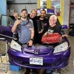 Marty from Mighty Car Mods, Dave from Haltech, Linus from Linus Tech Tips and Brian from VTEC Academy and Hasport Performance stand in the empty engine bay ready to install a K24 swap.