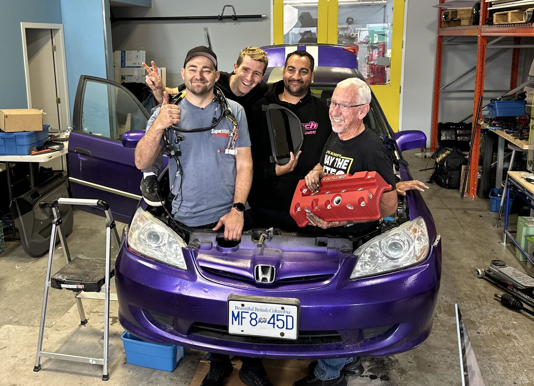 Marty from Mighty Car Mods, Dave from Haltech, Linus from Linus Tech Tips and Brian from VTEC Academy and Hasport Performance stand in the empty engine bay ready to install a K24 swap.